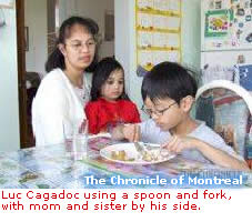 Luc Cagadoc using a spoon and fork, with mom and sister by his side. 