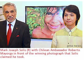 Mark Joseph Solis (R) poses with Chilean Ambassador Roberto Mayorga in front of the winning photo he claimed he took